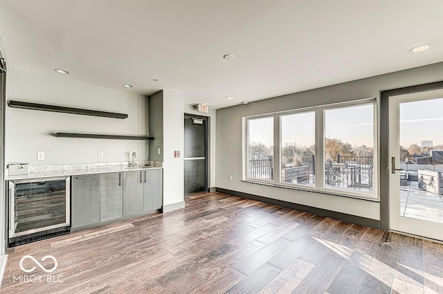 bar featuring wood finished floors, beverage cooler, baseboards, recessed lighting, and a sink