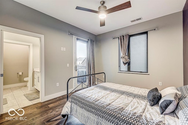 bedroom featuring a ceiling fan, wood finished floors, visible vents, baseboards, and ensuite bathroom