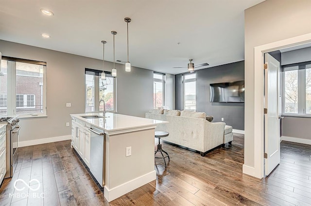 kitchen with an island with sink, a sink, dark wood finished floors, stainless steel appliances, and white cabinets