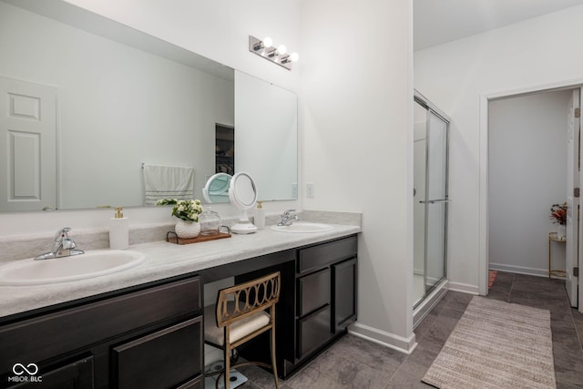 full bathroom featuring double vanity, a stall shower, baseboards, and a sink