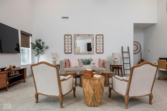 living area with light carpet, visible vents, and a high ceiling