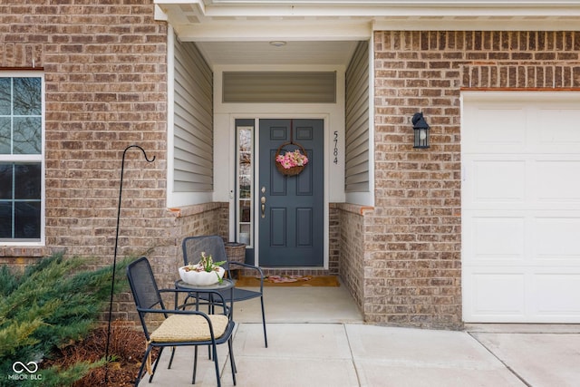 view of exterior entry featuring a garage and brick siding