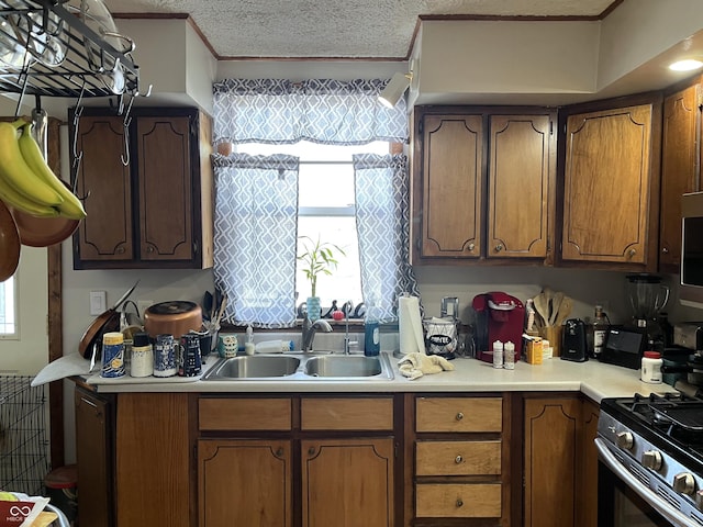 kitchen featuring crown molding, light countertops, a sink, a textured ceiling, and gas range