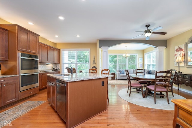 kitchen with light stone counters, appliances with stainless steel finishes, light wood-style floors, a sink, and ornate columns