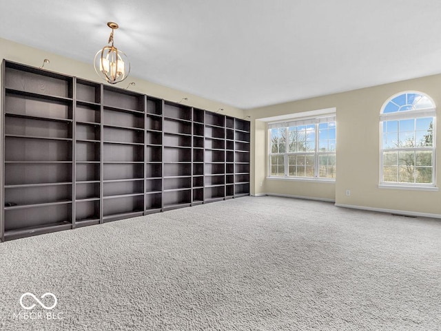 spare room with carpet floors, a notable chandelier, plenty of natural light, and baseboards