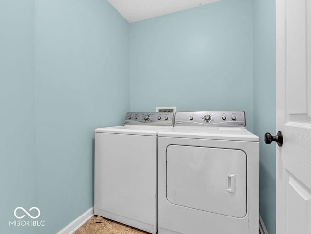 washroom featuring light tile patterned floors, laundry area, washing machine and clothes dryer, and baseboards