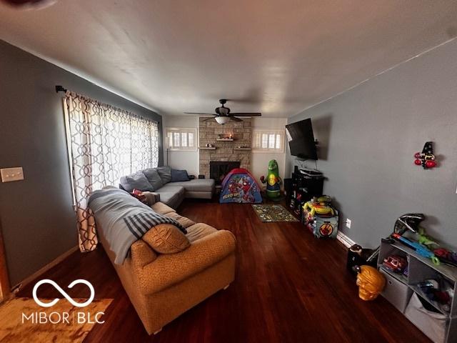 living room with a ceiling fan, a stone fireplace, baseboards, and wood finished floors