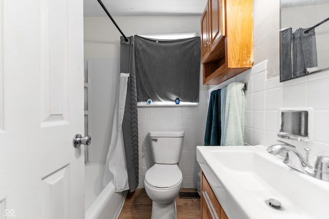 bathroom with toilet, wood finished floors, tile walls, shower / bath combination with curtain, and vanity