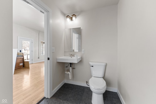 half bathroom featuring a sink, toilet, baseboards, and wood finished floors