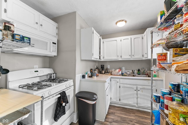 kitchen with white appliances, a sink, light countertops, dark wood-type flooring, and white cabinetry