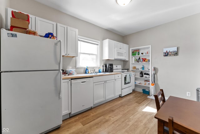 kitchen with light wood finished floors, light countertops, white cabinets, white appliances, and a sink