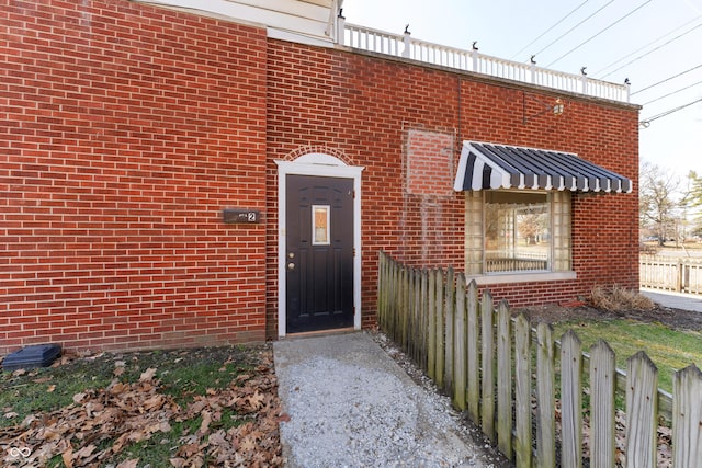 view of exterior entry with brick siding and fence