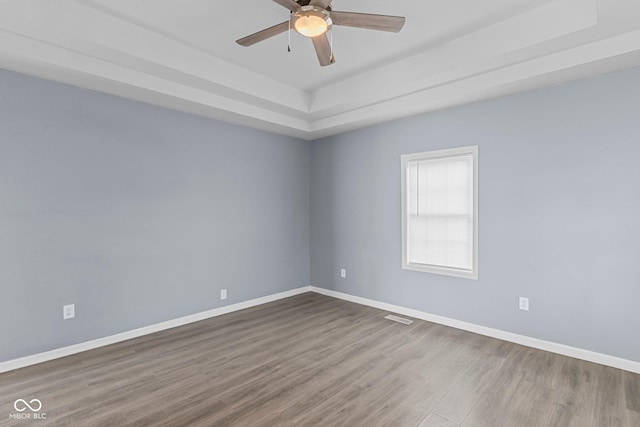 spare room featuring ceiling fan, wood finished floors, visible vents, baseboards, and a raised ceiling