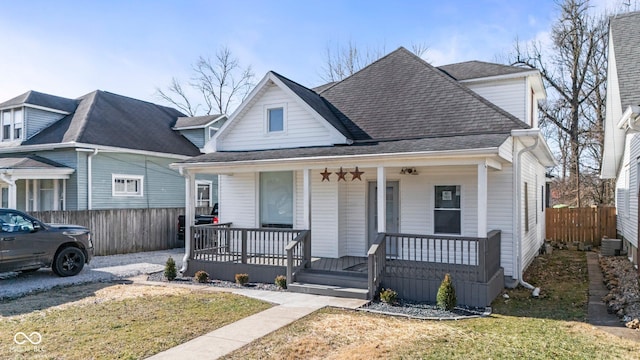 bungalow-style home featuring a porch, a shingled roof, and fence