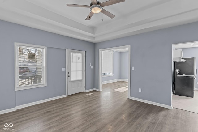 entrance foyer with ceiling fan, a tray ceiling, wood finished floors, and baseboards