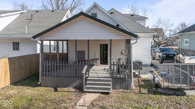 rear view of property with a porch, roof with shingles, and fence