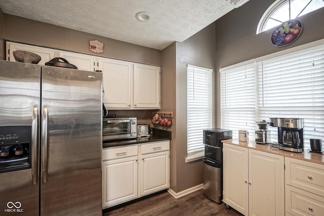 kitchen with a wealth of natural light, a textured ceiling, stainless steel fridge with ice dispenser, and white cabinetry