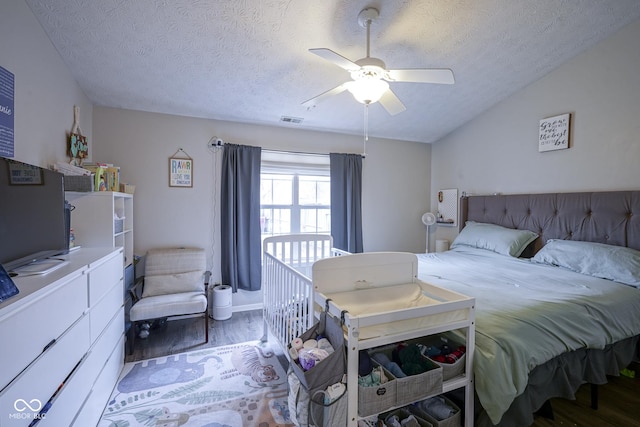 bedroom with visible vents, a ceiling fan, a textured ceiling, wood finished floors, and vaulted ceiling