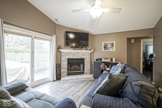 living area featuring visible vents, a textured ceiling, wood finished floors, lofted ceiling, and a brick fireplace