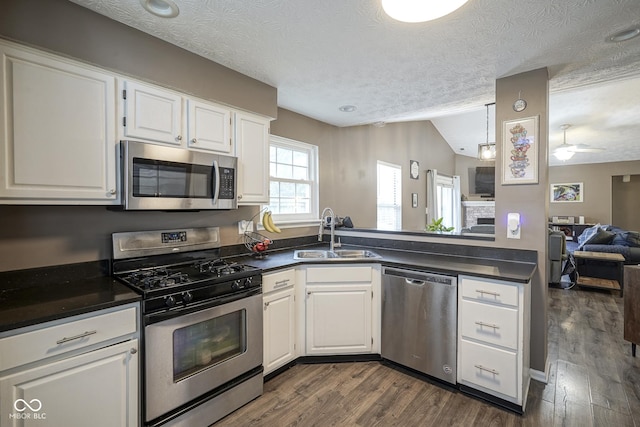 kitchen with lofted ceiling, a sink, stainless steel appliances, dark wood-type flooring, and dark countertops