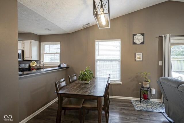 dining room with dark wood-style floors, visible vents, baseboards, vaulted ceiling, and a textured ceiling