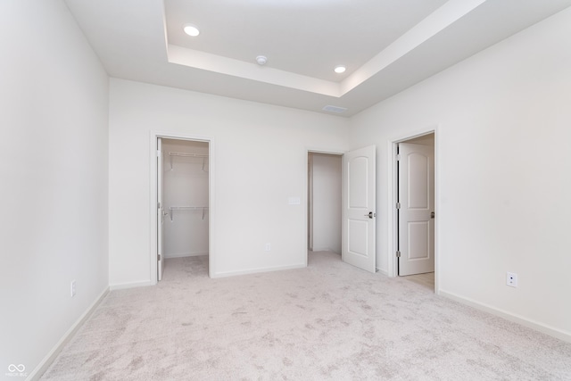 unfurnished bedroom with light colored carpet, a raised ceiling, and baseboards