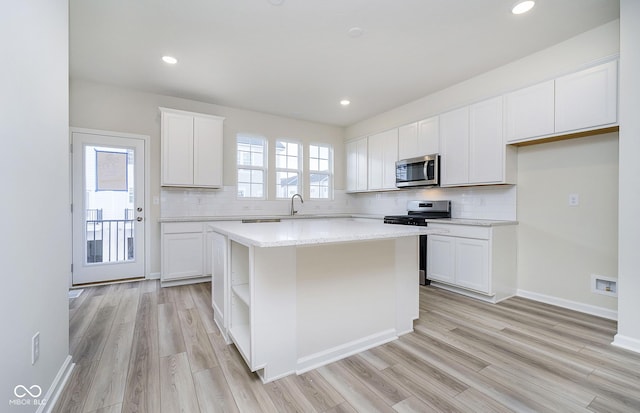 kitchen with backsplash, a kitchen island, white cabinets, stainless steel appliances, and a sink