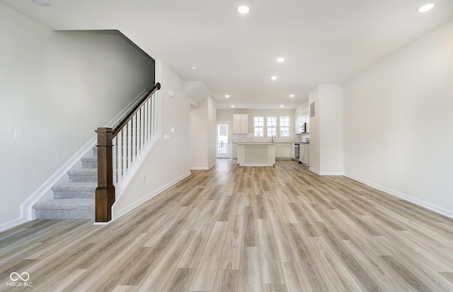 unfurnished living room featuring light wood-type flooring, stairway, baseboards, and recessed lighting