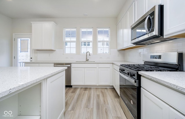 kitchen with light wood-style flooring, a sink, stainless steel appliances, decorative backsplash, and light stone countertops