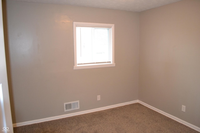 empty room featuring dark colored carpet, visible vents, and baseboards