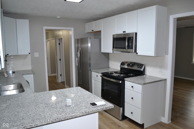 kitchen featuring light wood finished floors, appliances with stainless steel finishes, light stone countertops, white cabinetry, and a sink