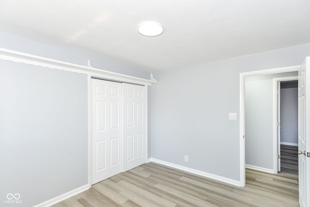 unfurnished bedroom featuring light wood-style floors, baseboards, and a closet