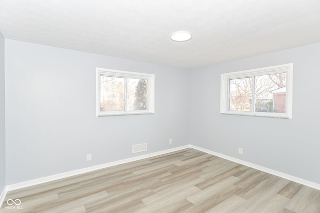 unfurnished room with light wood-type flooring, visible vents, plenty of natural light, and baseboards