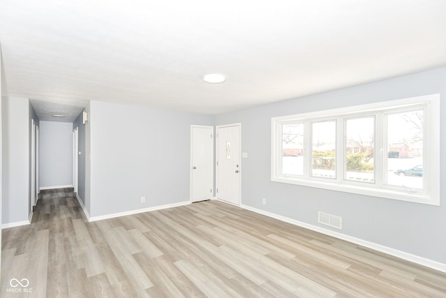 empty room with light wood-type flooring, visible vents, and baseboards