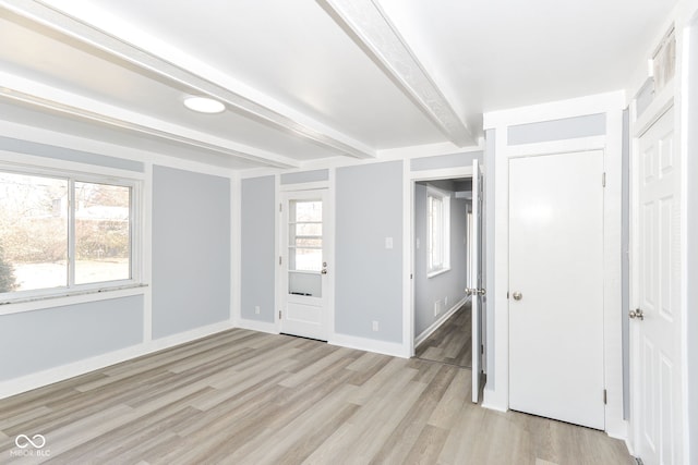 unfurnished room with light wood-style floors, beam ceiling, a healthy amount of sunlight, and baseboards