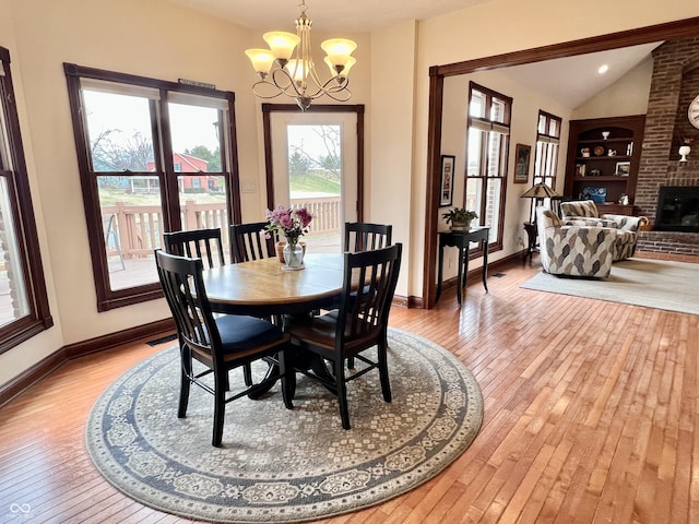 dining area with baseboards, built in features, light wood-type flooring, a fireplace, and a notable chandelier