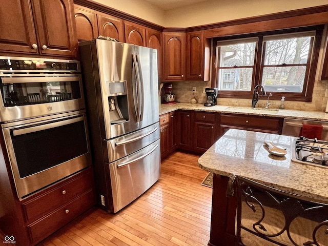 kitchen with stainless steel appliances, a sink, light wood-type flooring, decorative backsplash, and light stone countertops