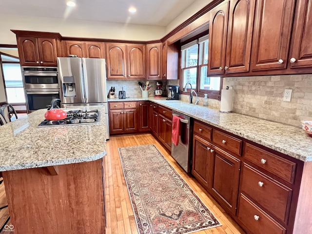 kitchen featuring light wood finished floors, a kitchen island, light stone counters, stainless steel appliances, and a sink