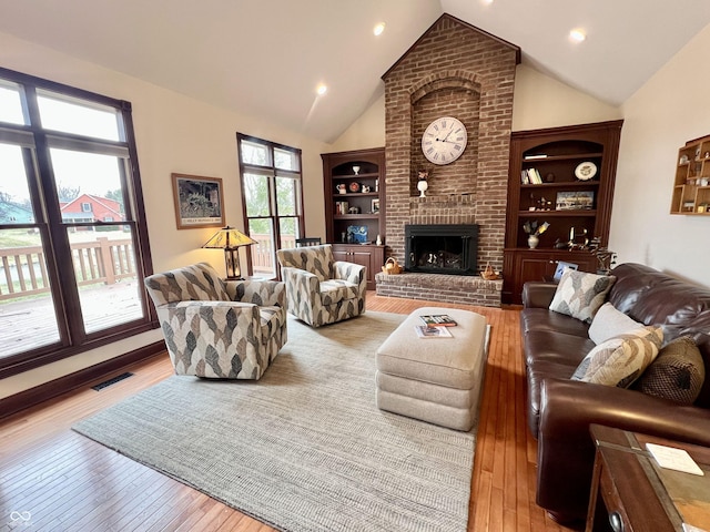 living room with visible vents, light wood-type flooring, a brick fireplace, built in shelves, and high vaulted ceiling