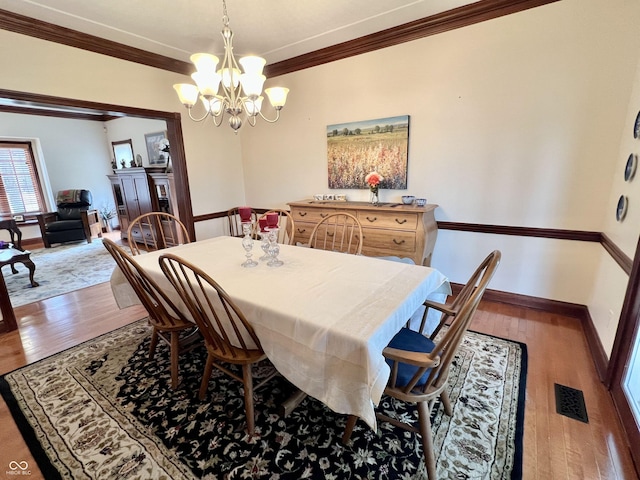 dining area featuring a notable chandelier, visible vents, hardwood / wood-style floors, ornamental molding, and baseboards