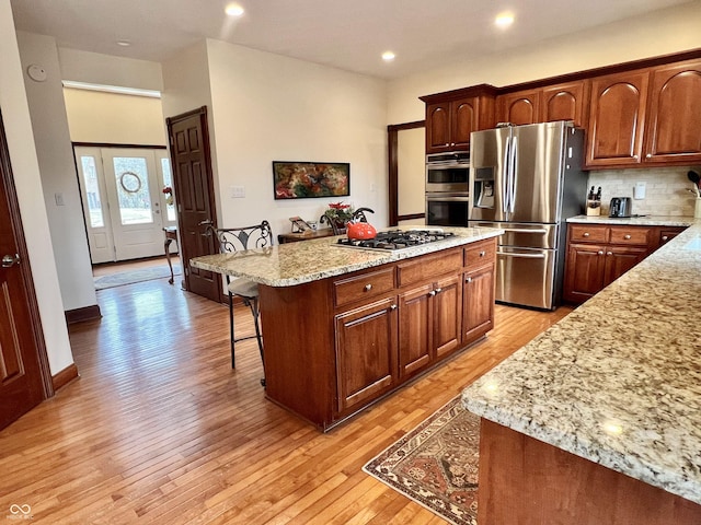 kitchen featuring stainless steel appliances, backsplash, a kitchen island, light wood-type flooring, and a kitchen breakfast bar