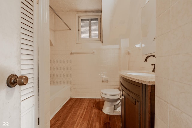 bathroom with toilet, vanity, wood finished floors, tile walls, and  shower combination