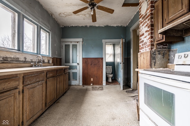 kitchen with under cabinet range hood, wainscoting, electric range, a ceiling fan, and a sink