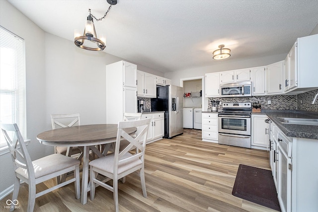 kitchen featuring washing machine and clothes dryer, dark countertops, tasteful backsplash, light wood-style floors, and stainless steel appliances