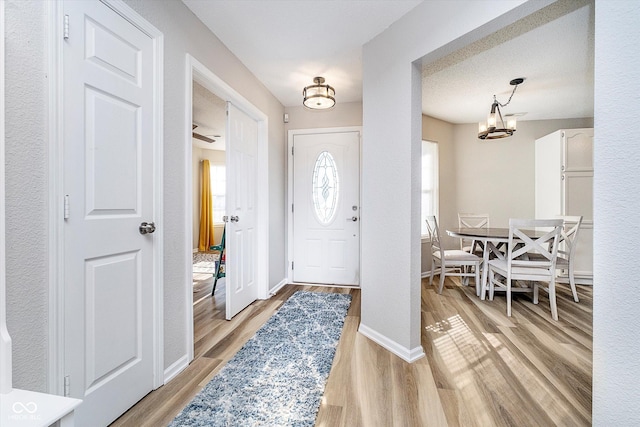 entryway with light wood finished floors, a notable chandelier, and baseboards