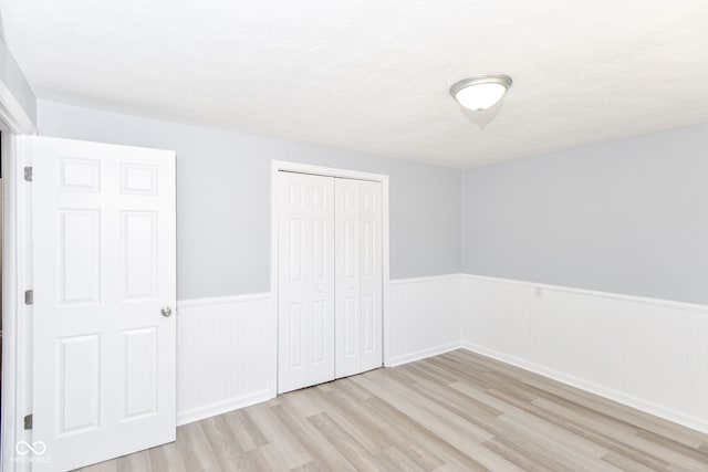 unfurnished bedroom featuring a closet, a wainscoted wall, a textured ceiling, and wood finished floors