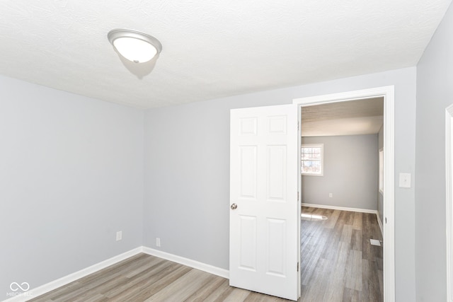 unfurnished bedroom featuring light wood-style flooring, baseboards, and a textured ceiling