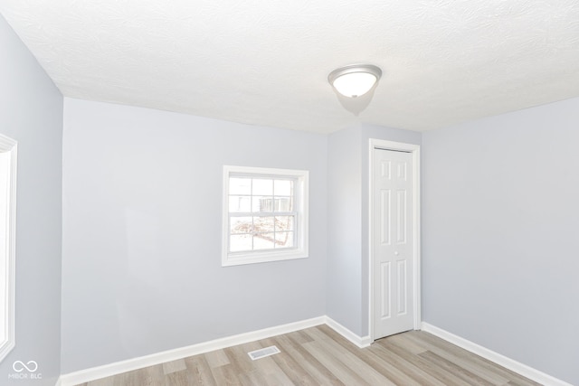 spare room featuring light wood-style floors, baseboards, visible vents, and a textured ceiling