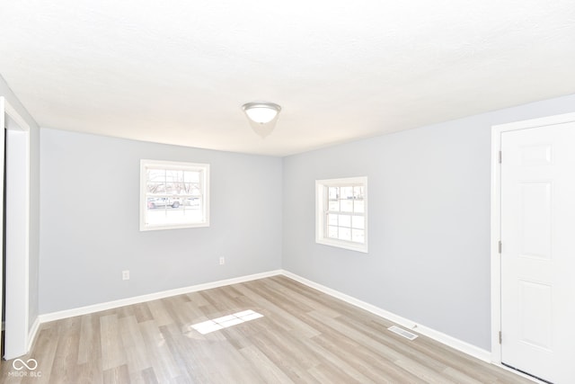 unfurnished room featuring a textured ceiling, light wood-style floors, visible vents, and baseboards