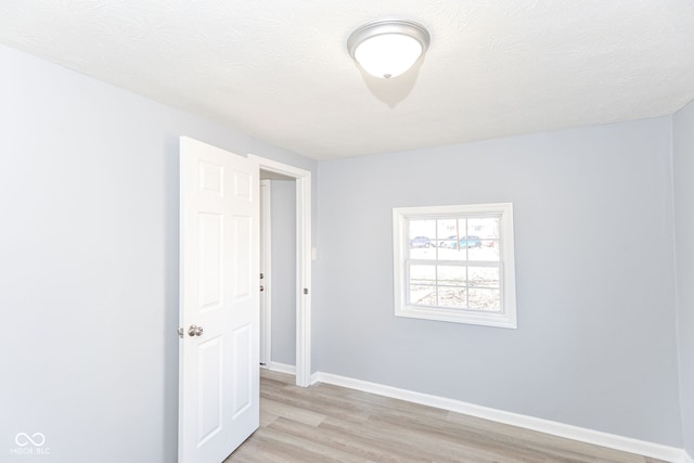 spare room with baseboards, a textured ceiling, and light wood finished floors